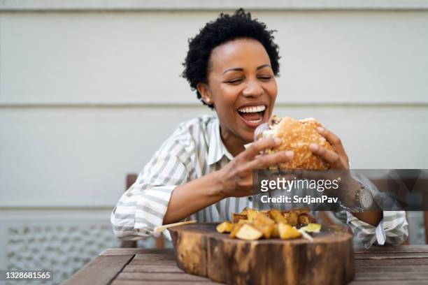 cheerful businesswoman enjoying in delicious burger with potato in a restaurant - woman eating burger stock pictures, royalty-free photos & images