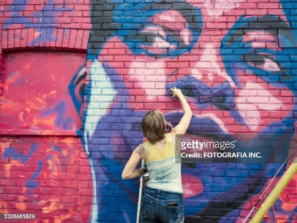 young woman painting mural on the house - painter artist stockfoto's en -beelden