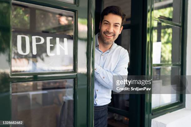 happy young restaurant owner hanging open sign on a door - opening event stock pictures, royalty-free photos & images