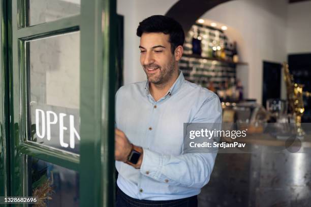 hübscher junger restaurantbesitzer, der ein offenes schild an einer tür hängt - geschäftseröffnung stock-fotos und bilder