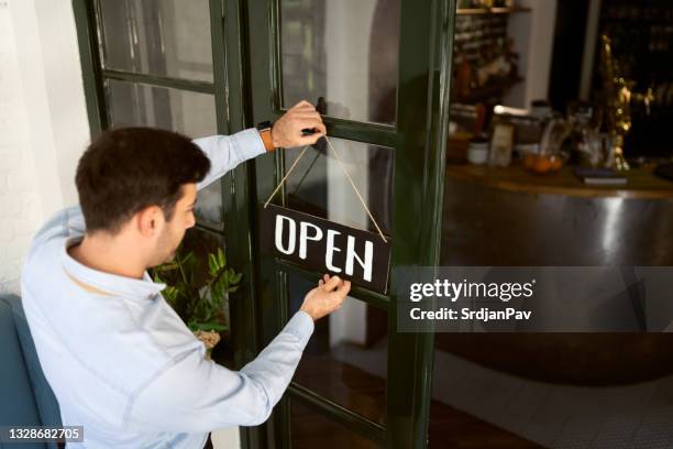 hochwinkelansicht eines jungen restaurantbesitzers, der ein offenes schild an einer tür aufhängt - open sign on door stock-fotos und bilder