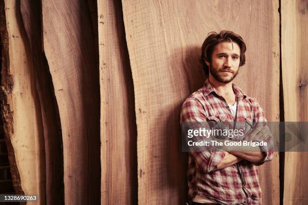 portrait of carpenter standing against wood planks in workshop - checked shirt stock-fotos und bilder