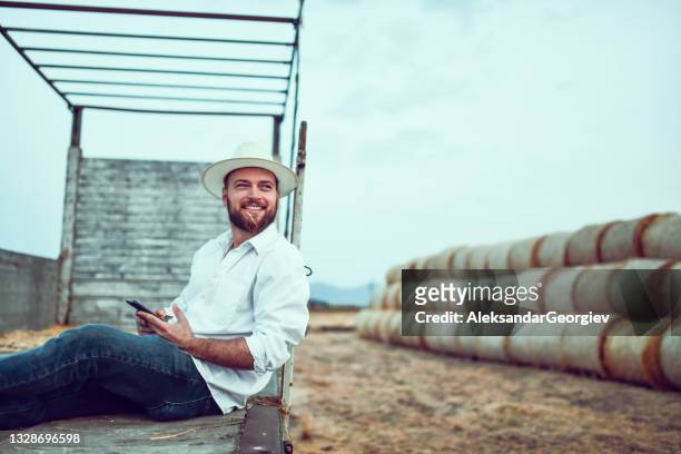 agriculteur souriant se relaxant dans un chariot de camion en attendant que les travailleurs chargent des balles de foin - agriculteur selfie photos et images de collection