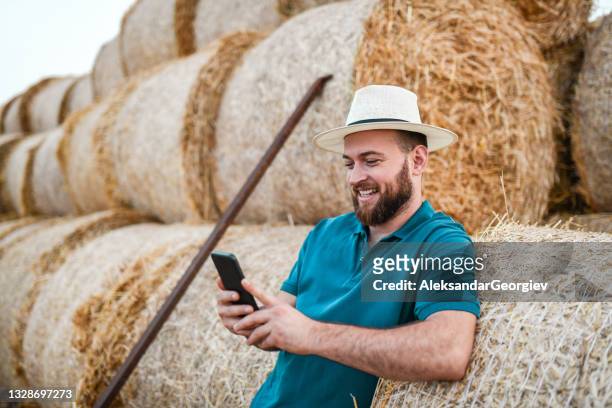 agriculteur souriant se relaxant avec un smartphone tout en s’énant sur des balles de foin - agriculteur selfie photos et images de collection