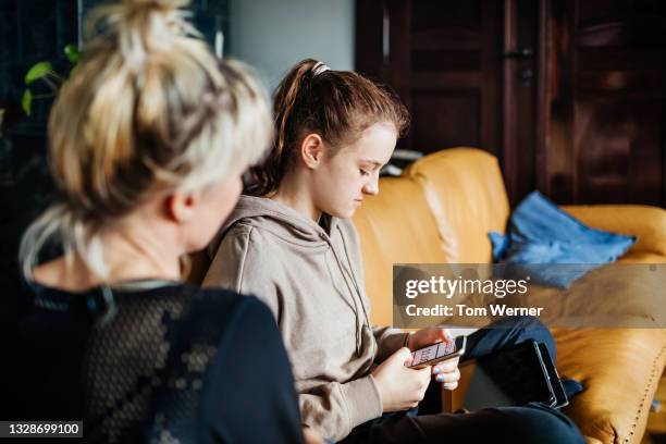 teenager sitting on couch texting next to mom - teen girl 15 sitting fotografías e imágenes de stock
