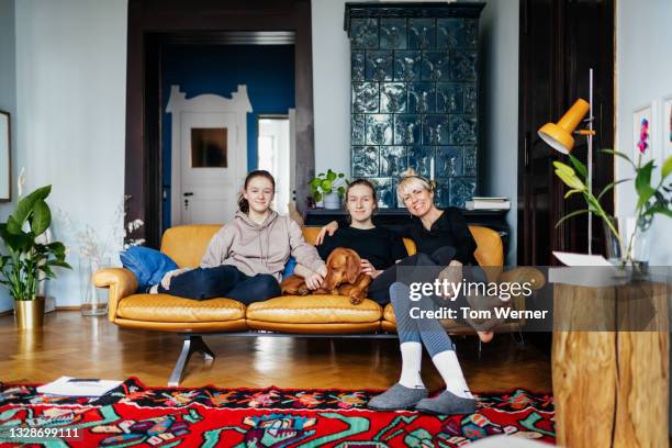 portrait of single mom sitting with two daughters - family sofa stock-fotos und bilder