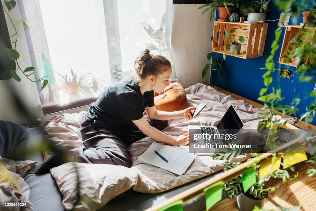 Teenage Girl Studying In Bedroom Using Zoom On Laptop