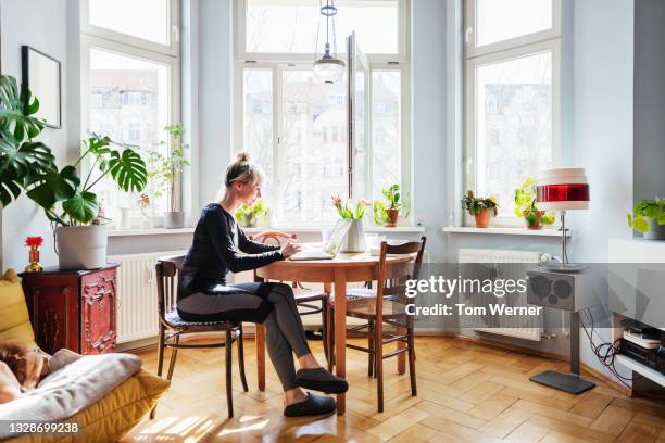 single mom sitting in living room using laptop - überkreuzte beine stock-fotos und bilder