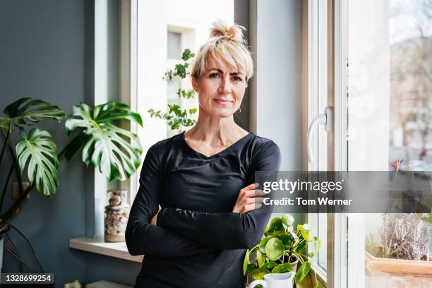 portrait of single mom standing by living room window - gente mayor fotografías e imágenes de stock