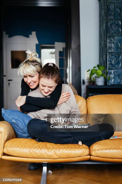single mom hugging daughter sitting on sofa - mother daughter couch imagens e fotografias de stock