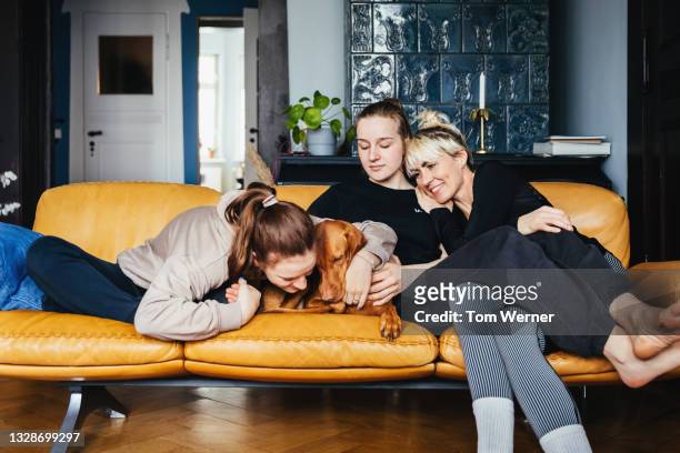 Single Mom Sitting With Daughters And Family Dog On Sofa Togehter