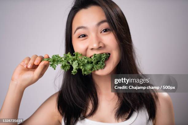 happy asian woman eating healthy kale salad against white background - hate broccoli stock pictures, royalty-free photos & images