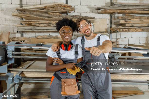 un couple satisfait de charpentiers multiculturels sourit à la caméra dans un atelier spacieux. - artisan portrait equipe photos et images de collection