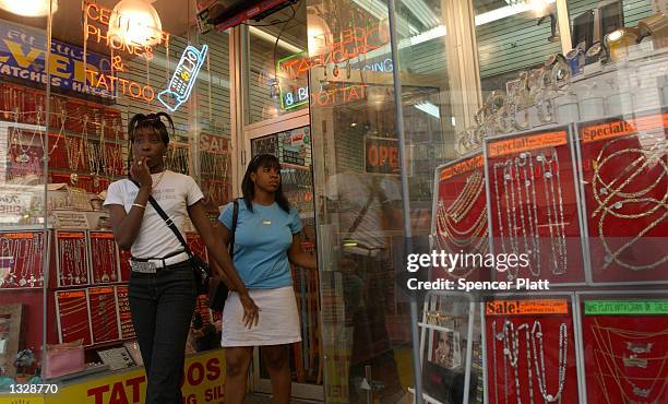 Women walk out of one of numerous stores that sell removable gold tooth caps, or fronts as they are called on the street, June 29, 2001 in Brooklyn,...