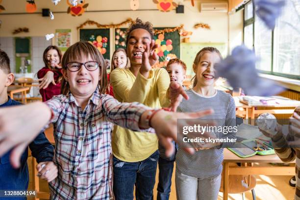 happy school children throwing crumpled papers towards the camera. - aggression school stock pictures, royalty-free photos & images