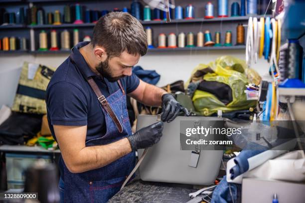young man in crafts repair shop pulling strap through buckle on women's purse - leather strap stock pictures, royalty-free photos & images