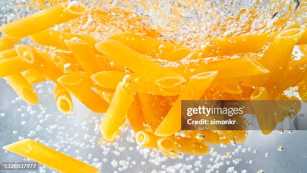 penne pasta falling into boiling water - boiling pasta stock pictures, royalty-free photos & images