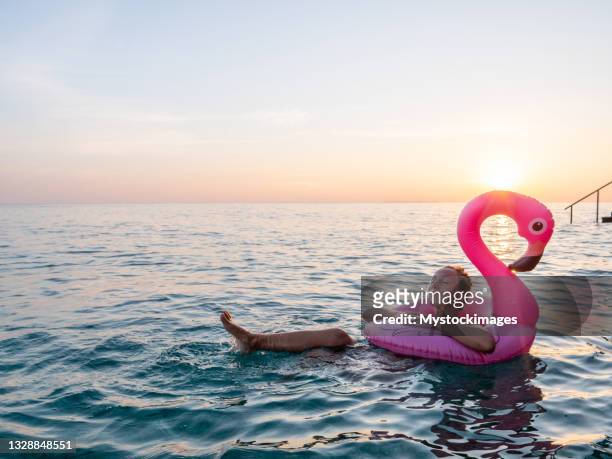 junge frau beobachtet den sonnenaufgang von ihrem schwimmenden flamingo aus - flamingos stock-fotos und bilder