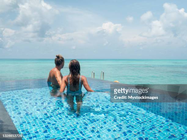 paar schwimmen im infinity-pool über der tropischen lagune - infinity pool stock-fotos und bilder