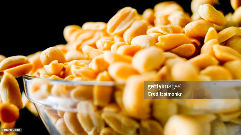 Roasted peanuts overflowing from glass bowl