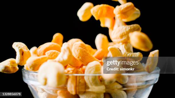 geröstete cashewnüsse fallen in eine glasschüssel - cashewnuss stock-fotos und bilder