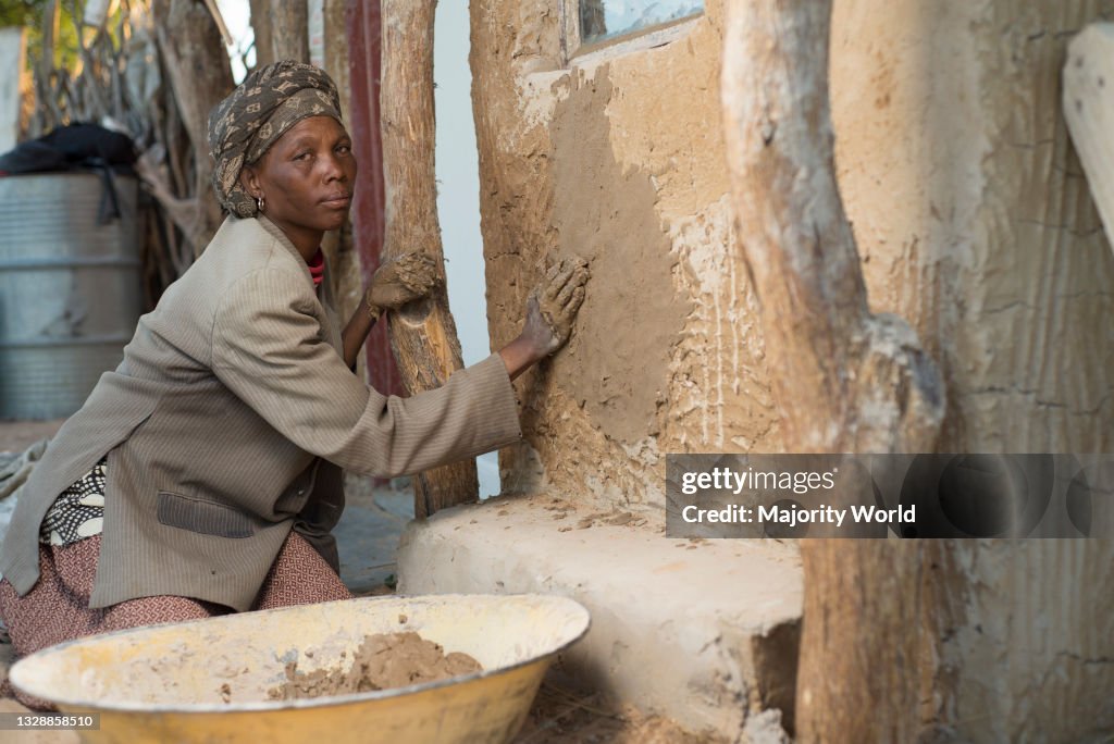 A woman plastering a traditional hut.
