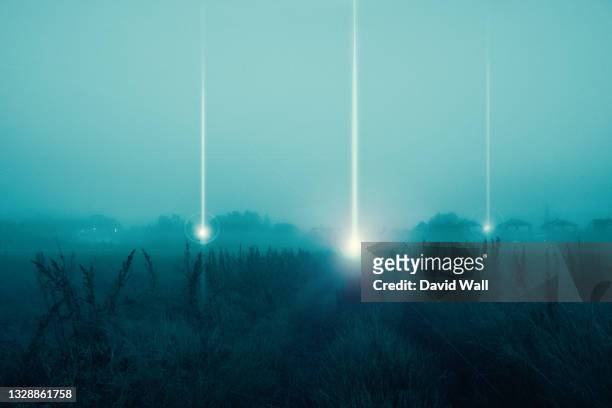 a moody science fiction concept, of ufo light beams landing in a field coming down from the sky. on a foggy spooky night. - science et technologie stock-fotos und bilder