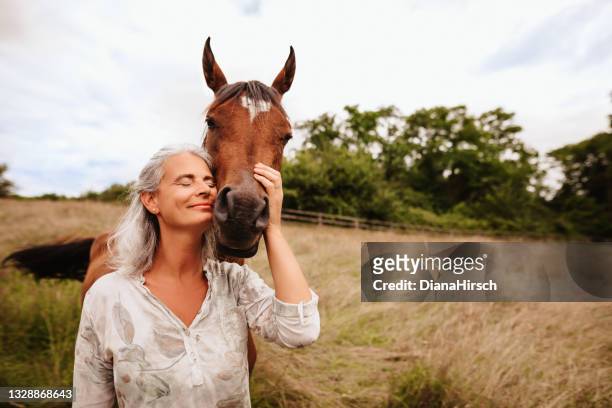 bella donna matura godendo a occhi chiusi la sua cavalla araba marrone nella natura libera - cavallo equino foto e immagini stock