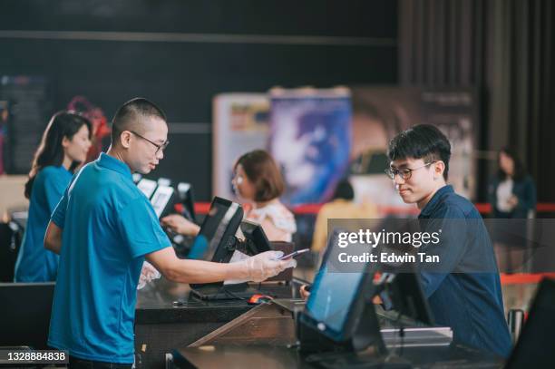 joven chino asiático ordenando agua mineral de palomitas de maíz en el mostrador del bar en el cine antes de la hora del espectáculo de cine - ticket counter fotografías e imágenes de stock