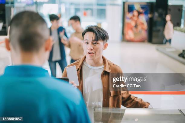 el público masculino joven chino asiático en el mostrador de boletos delantero comprando boletos de cine y palomitas de maíz beben el pago sin contacto antes de la hora del espectáculo de cine en el cine de cine - taquilla lugar de comercio fotografías e imágenes de stock