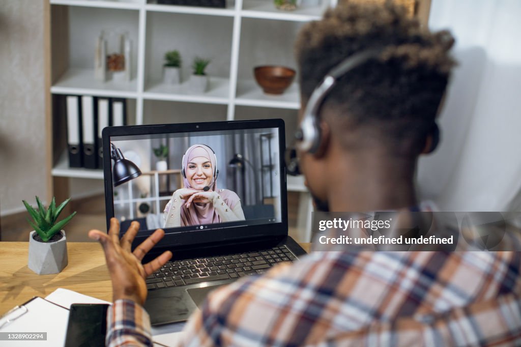 Hombre africano que tiene video chat en la computadora portátil con la mujer musulmana