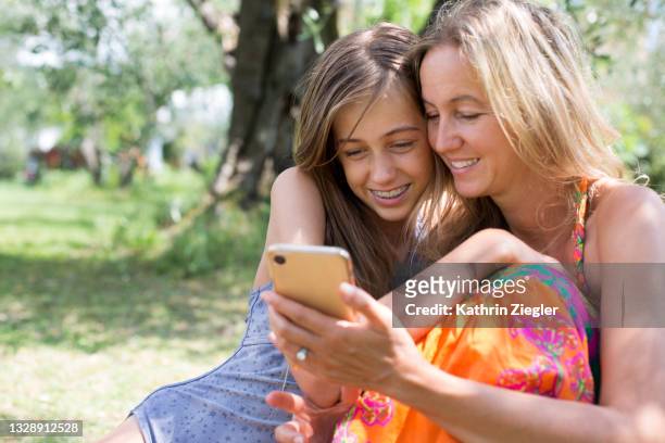 mother and pre-adolescent daughter looking at smartphone together - adult retainer stock-fotos und bilder