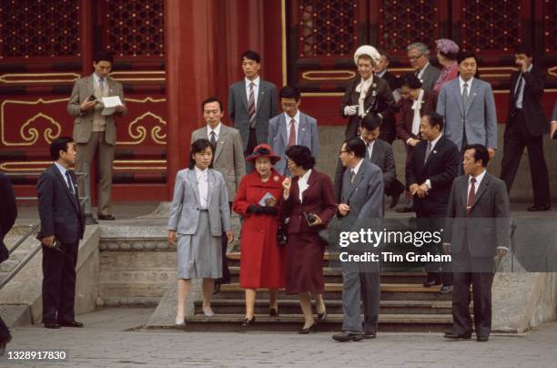 British Royal Queen Elizabeth II, wearing a red coat with a red hat which features a black band with a black floral motif, walking with First Lady of...