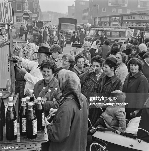 Women queuing at a sarsaparilla drink stand at East Street Market in Walworth, southeast London, UK, 28th October 1965.