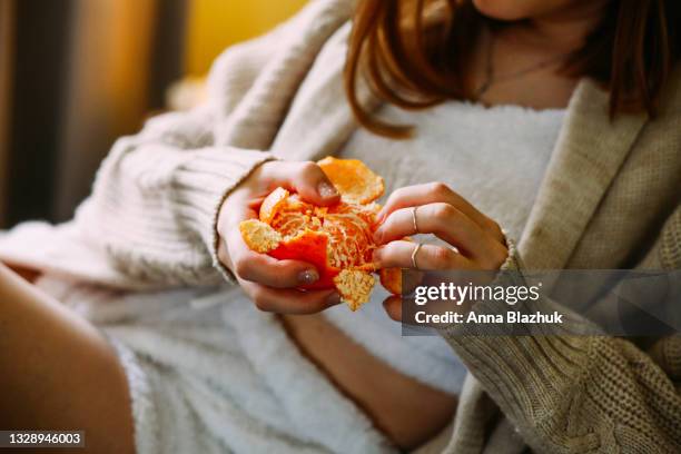 close-up of woman's hand holding and eating tangerine at home. - woman eating fruit imagens e fotografias de stock