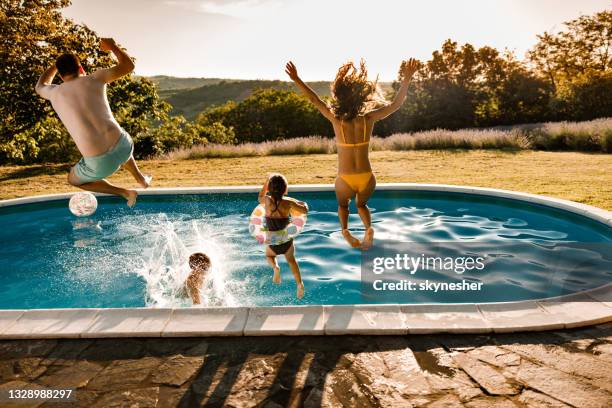 vista trasera de la familia despreocupada saltando en la piscina en el patio trasero. - jardín de detrás fotografías e imágenes de stock