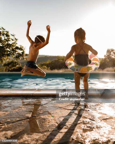 verspielte geschwister, die sich am sommertag am pool vergnügen. - jump in pool stock-fotos und bilder