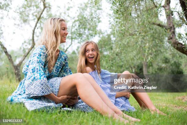 mother and daughter sitting on grass, laughing - sommerkleid stock-fotos und bilder