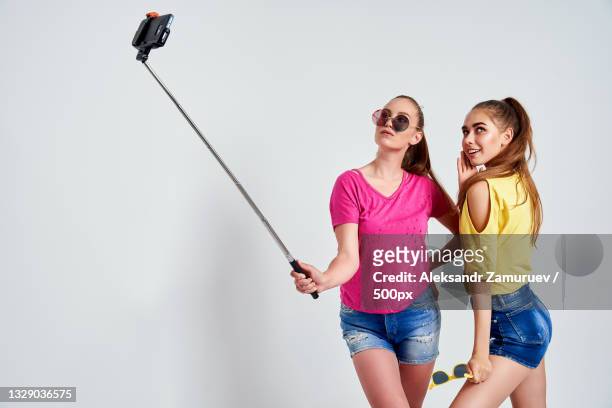 female friends holding camera while standing against white background - selfie stick white background stock-fotos und bilder