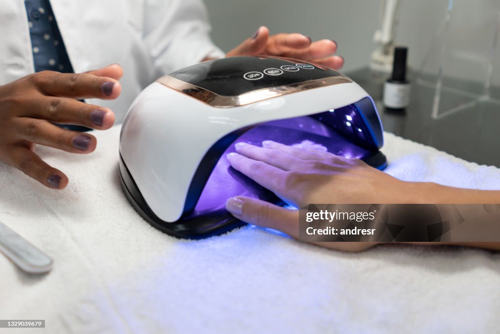 Mujer que consigue una manicura semipermanente y secando el esmalte de uñas con una lámpara UV