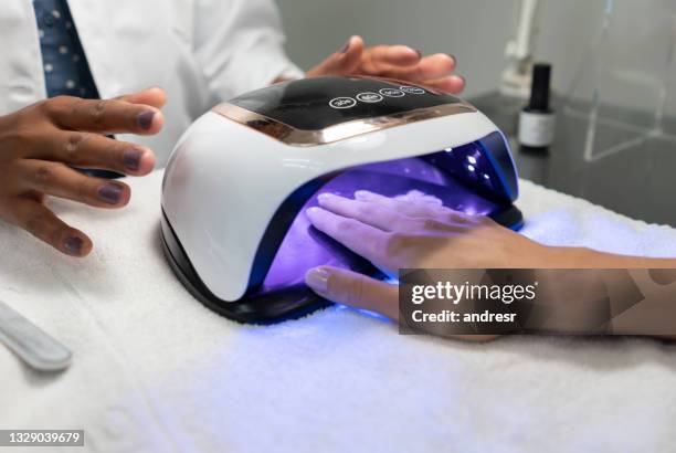 woman getting a semi-permanent manicure and drying the nail polish with a uv lamp - nail polish stockfoto's en -beelden