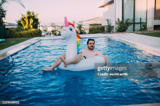 man on inflatable unicorn float in swimming pool - float stockfoto's en -beelden