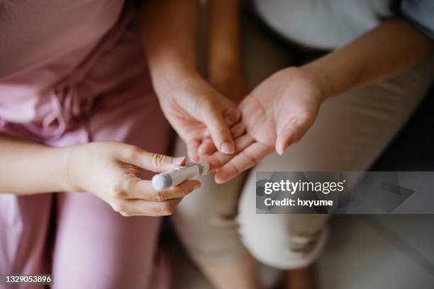 close-up woman helping her mother check blood sugar level at home - finger poking stock pictures, royalty-free photos & images