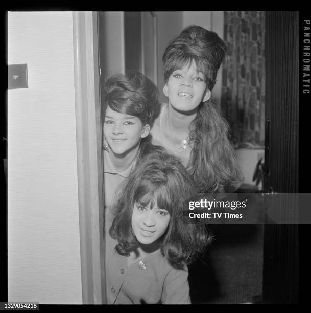 Estelle Bennett, Nedra Talley and Veronica Bennett of American pop/R&B group The Ronettes peering round a door frame, circa 1965.