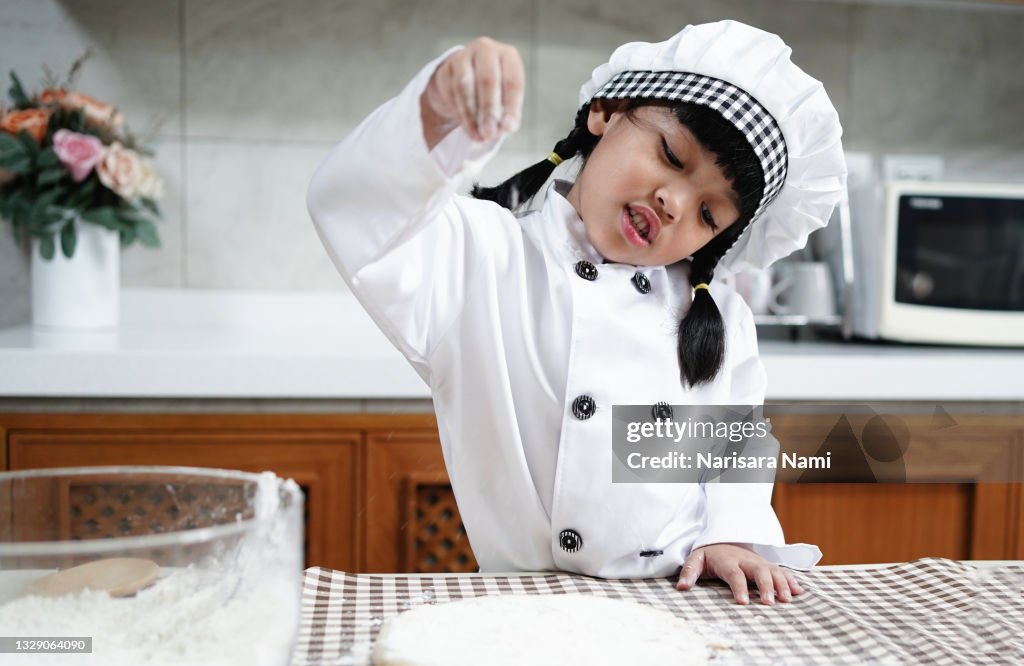 Asian chef kid child girl enjoys cooking in the kitchen. Happy Asian kids are preparing the dough, bake bakery in the kitchen.