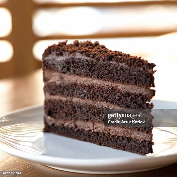 chocolate cake. piece of brown layered dessert with cream on white saucer. sunny blurred background. soft focus - slice cake stock pictures, royalty-free photos & images