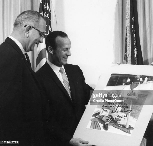 President Lyndon B Johnson looks on as retired baseball player Stan Musial presents him with an autographed photo, Washington DC, February 26, 1964....