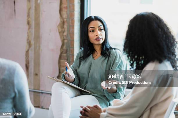 female therapist gestures while speaking to unrecognizable young adult woman - mental health professional stock pictures, royalty-free photos & images