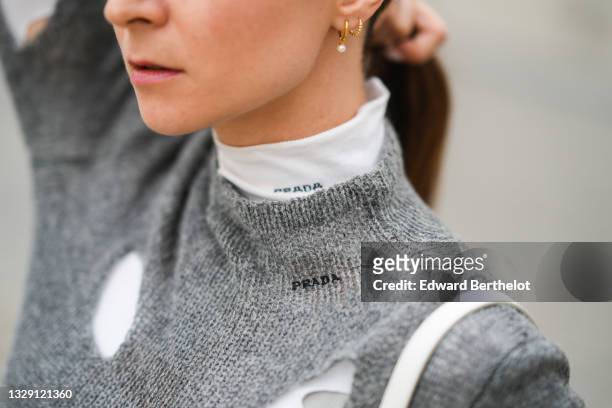 Julia Comil wears a gray wool sweater with holes by Prada, a white turtleneck top with holes by Prada, pear earrings, on July 15, 2021 in Paris,...