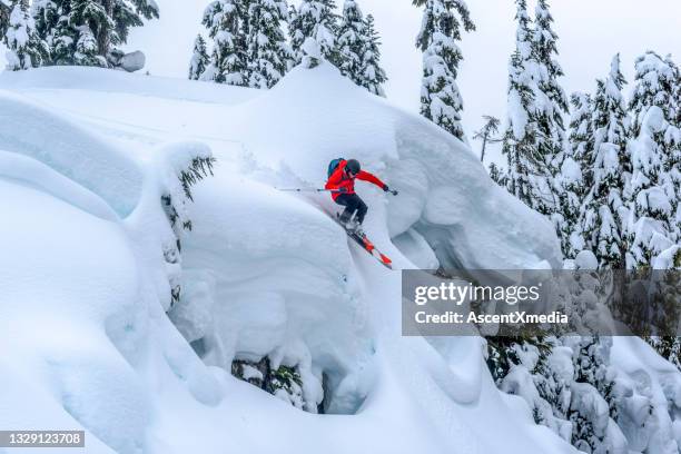 view of backcountry skier riding down steep, snowy cliff - telemark skiing stockfoto's en -beelden